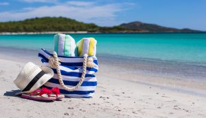 Beach bag, straw hat, towel on the white sandy tropical beach