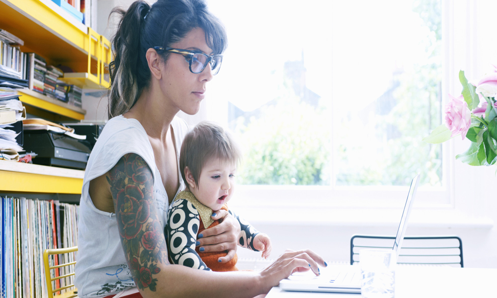 mother with baby in lap working on laptop at home